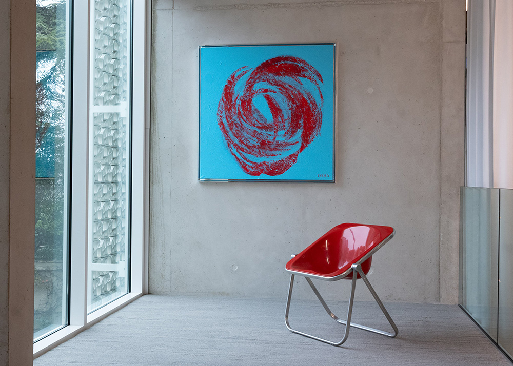 A modern interior featuring a red chair and an abstract artwork with red and blue tones, displayed on a concrete wall near a large window.