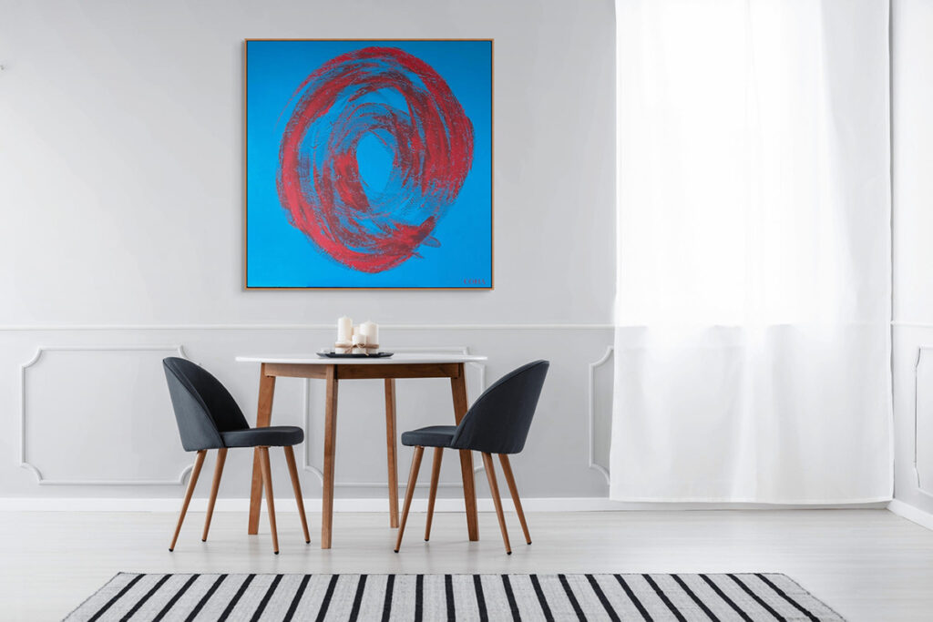 Abstract blue and red painting displayed in a minimalist room consisting of a table and two black chairs.